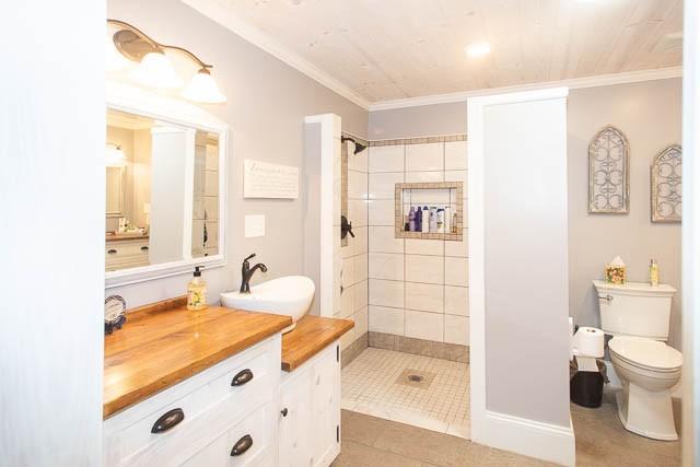 6684 Eudailey Covington Rd, College Grove, TN 37046 - bathroom with tiled shower, vanity, toilet, crown molding, and tile patterned flooring
