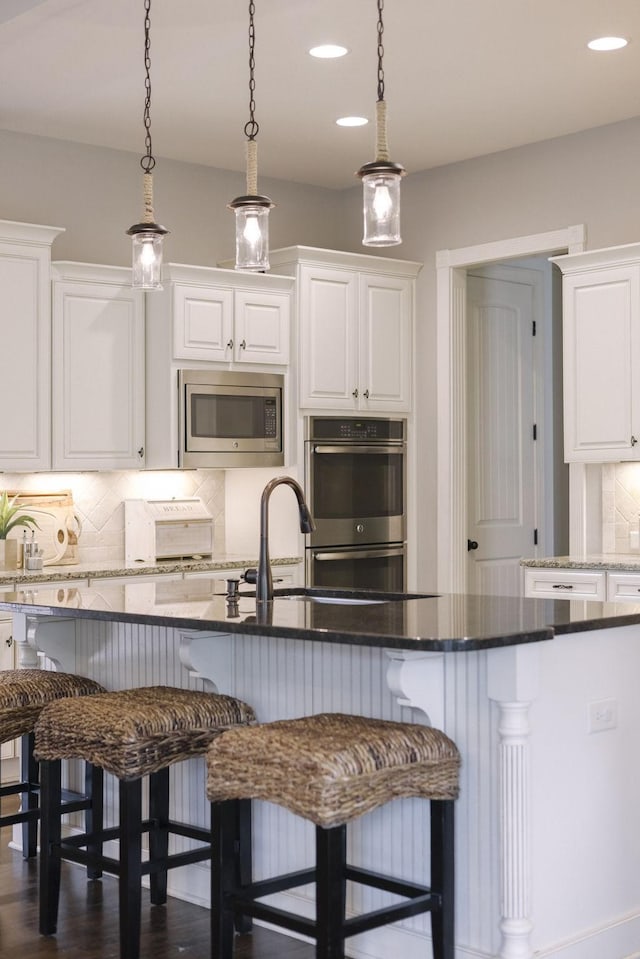 1825 Barnstaple Ln, Brentwood, TN 37027 - kitchen with appliances with stainless steel finishes, white cabinets, decorative backsplash, a breakfast bar, and recessed lighting