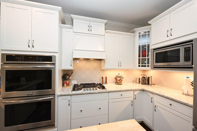 146 Monarchos Dr, Gallatin, TN 37066 - kitchen featuring appliances with stainless steel finishes, premium range hood, white cabinetry, tasteful backsplash, and ornamental molding