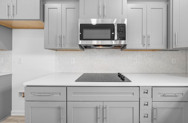 2582 Rafiki Dr, Clarksville, TN 37042 - kitchen with stainless steel microwave, gray cabinets, black electric stovetop, light countertops, and decorative backsplash