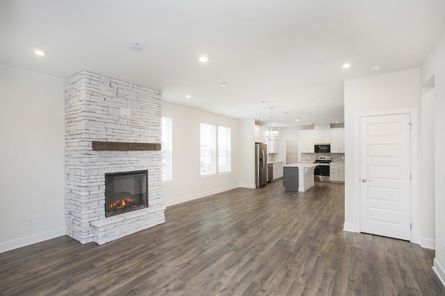 3013 Kemp Dr, Hermitage, TN 37076 - unfurnished living room with a stone fireplace, dark wood-type flooring, baseboards, recessed lighting, and a chandelier