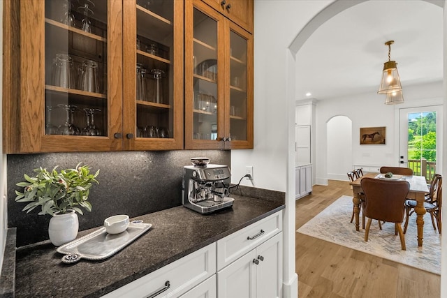 1750 Barrow Ln, Brentwood, TN 37027 - kitchen featuring arched walkways, glass insert cabinets, light wood-type flooring, dark stone countertops, and white cabinets
