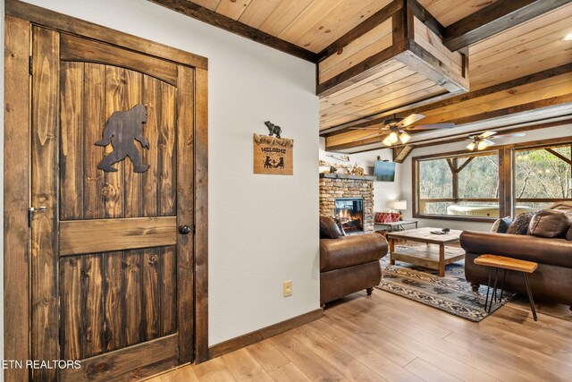817 Pine Top Ln, Gatlinburg, TN 37738 - living area featuring light wood-style floors, wooden ceiling with exposed beams, a stone fireplace, ceiling fan, and baseboards