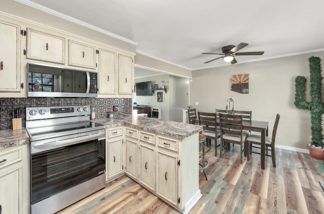 235 Pinecrest Dr, Henderson, TN 38340 - kitchen featuring appliances with stainless steel finishes, a peninsula, cream cabinets, a ceiling fan, and backsplash