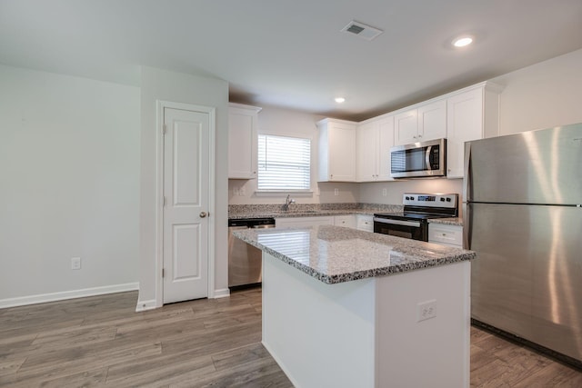 1003 Autumnwood Dr, Dickson, TN 37055 - kitchen featuring stainless steel appliances, white cabinets, light stone counters, a center island, and light wood-style floors