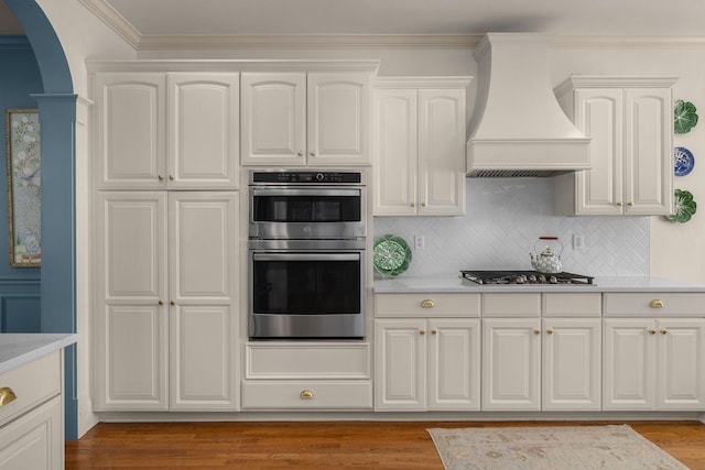 403 Butterfly Ct, Franklin, TN 37069 - kitchen featuring wall chimney exhaust hood, stainless steel appliances, arched walkways, light countertops, and ornamental molding