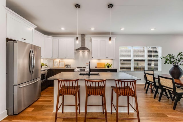 600B 41st Ave N, Nashville, TN 37209 - kitchen with appliances with stainless steel finishes, wall chimney exhaust hood, a sink, light wood finished floors, and a breakfast bar area