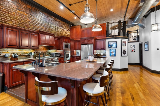 207 3rd Ave N Unit 602, Nashville, TN 37201 - kitchen featuring stainless steel appliances, reddish brown cabinets, a sink, premium range hood, and a high ceiling