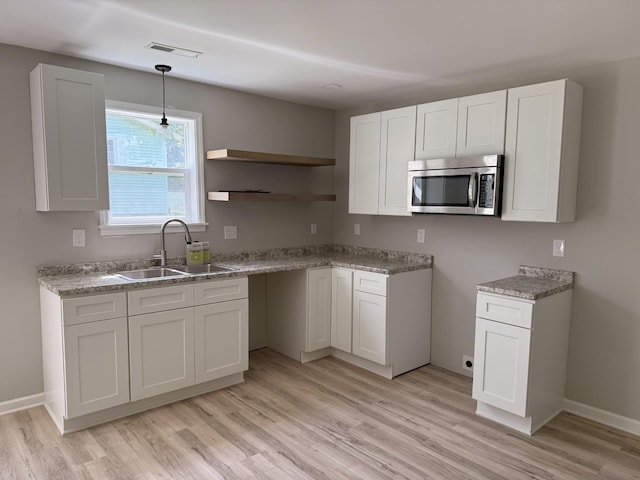 711 Gwen St, Paris, TN 38242 - kitchen featuring stainless steel microwave, light wood-type flooring, white cabinetry, and hanging light fixtures