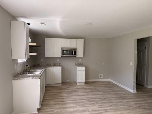711 Gwen St, Paris, TN 38242 - kitchen featuring stainless steel microwave, open shelves, light wood-style flooring, and white cabinets