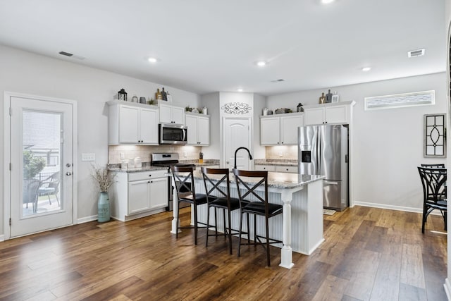 1045 Brayden Dr, Fairview, TN 37062 - kitchen featuring stainless steel appliances, decorative backsplash, white cabinets, a kitchen bar, and a kitchen island with sink