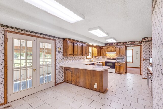 220 Winton Way Rd, Manchester, TN 37355 - kitchen with wallpapered walls, white electric stove, brown cabinets, a peninsula, and under cabinet range hood