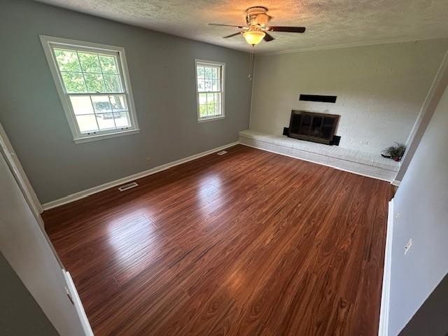 203 Arnold Ave, Tullahoma, TN 37388 - unfurnished living room featuring a textured ceiling, ceiling fan, dark wood-type flooring, a brick fireplace, and baseboards