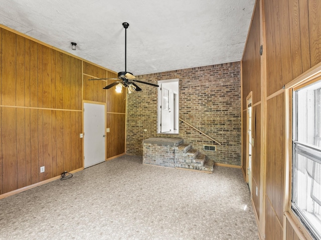1611 Lincoln St W, Tullahoma, TN 37388 - unfurnished living room with a ceiling fan, brick wall, wooden walls, and plenty of natural light