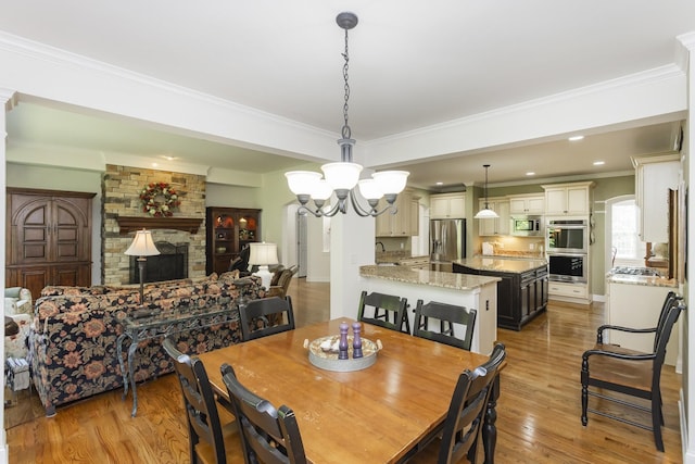 1414 Bernard Way, Franklin, TN 37067 - dining space featuring light wood-style flooring, a chandelier, ornamental molding, a stone fireplace, and recessed lighting