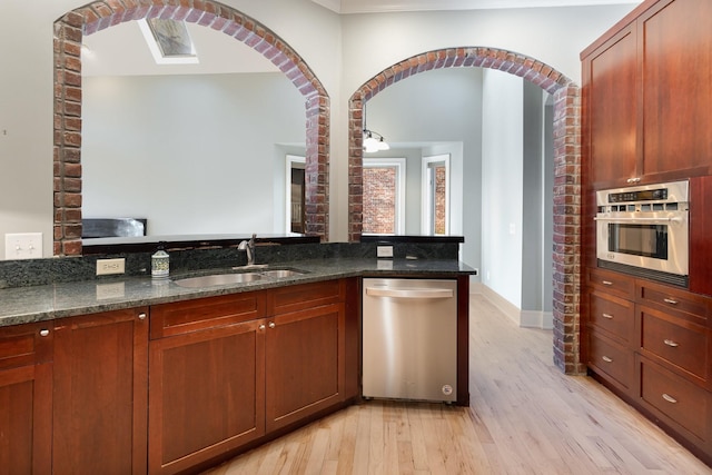 1107 Stonebridge Park Dr, Franklin, TN 37069 - kitchen with stainless steel appliances, a sink, arched walkways, light wood-style flooring, and dark stone counters