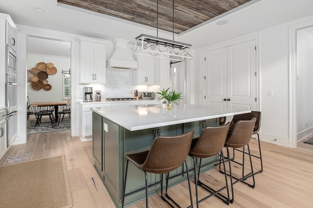 7546 Delancey Dr, College Grove, TN 37046 - kitchen featuring light wood-type flooring, white cabinetry, a kitchen island, custom range hood, and light countertops