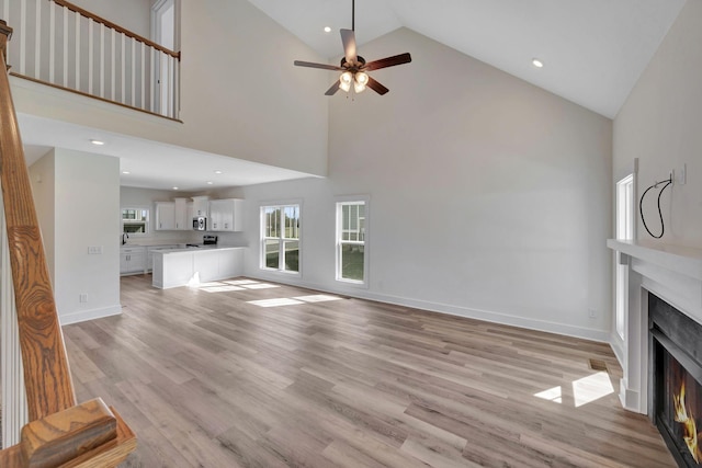 1038 Camden Trl, Greenbrier, TN 37073 - unfurnished living room with a warm lit fireplace, ceiling fan, high vaulted ceiling, light wood finished floors, and baseboards
