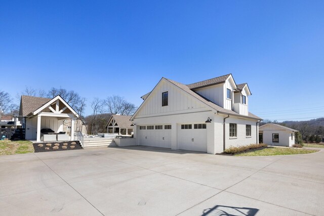 6115 Hillsboro Pike, Nashville, TN 37215 - view of home's exterior featuring board and batten siding, concrete driveway, a garage, a shingled roof, and brick siding