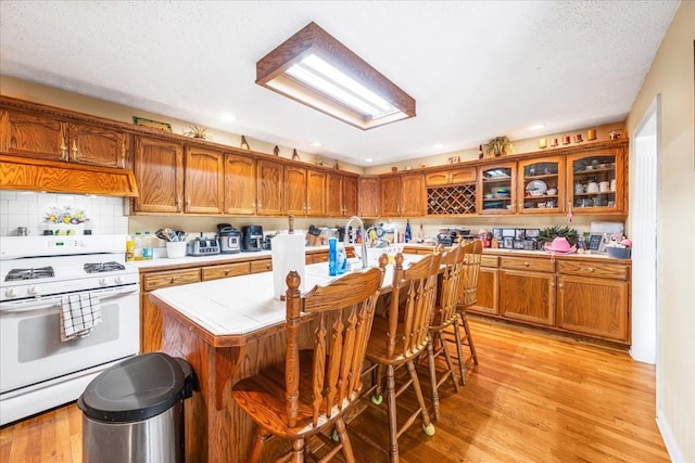 431 Jack Thomas Dr, Manchester, TN 37355 - kitchen featuring white range with gas cooktop, brown cabinetry, light wood finished floors, recessed lighting, and tile counters