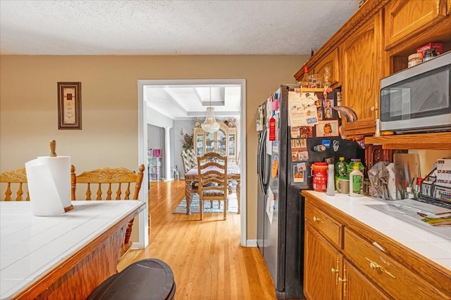 431 Jack Thomas Dr, Manchester, TN 37355 - kitchen featuring tile countertops, stainless steel microwave, light wood-type flooring, brown cabinets, and refrigerator with ice dispenser