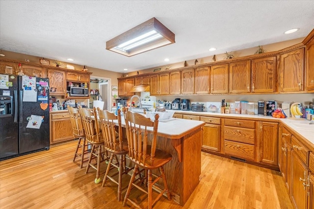 431 Jack Thomas Dr, Manchester, TN 37355 - kitchen featuring black fridge with ice dispenser, stainless steel microwave, light wood-style floors, light countertops, and brown cabinetry
