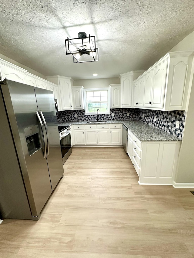 115 Briley Ln, Portland, TN 37148 - kitchen with stainless steel appliances, light wood-style floors, tasteful backsplash, white cabinets, and a textured ceiling