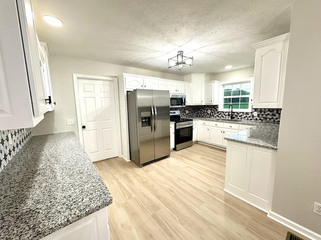 115 Briley Ln, Portland, TN 37148 - kitchen featuring stainless steel appliances, tasteful backsplash, white cabinets, light wood-style floors, and a textured ceiling