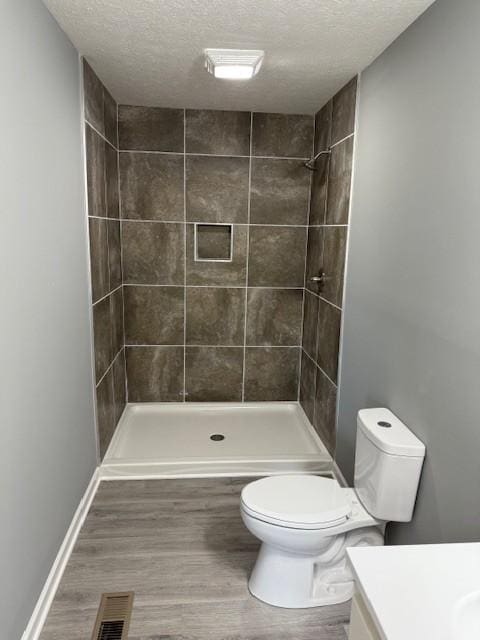 406 New Rock Creek Rd, Tullahoma, TN 37388 - bathroom featuring vanity, toilet, a textured ceiling, a tile shower, and wood finished floors