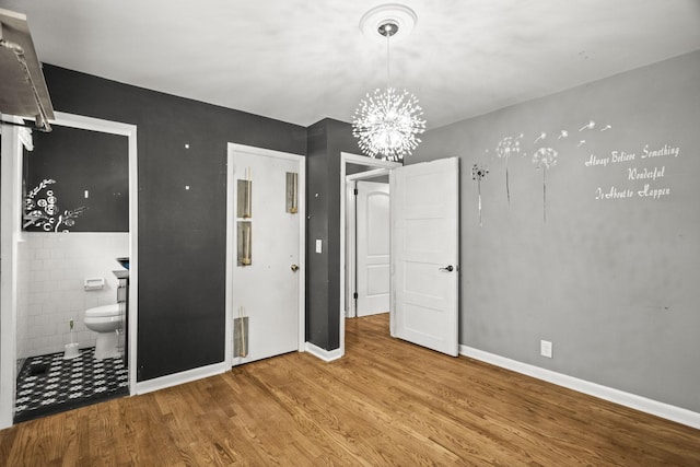 225 Nelson Dr, La Vergne, TN 37086 - unfurnished bedroom featuring a chandelier, wood finished floors, ensuite bath, tile walls, and baseboards