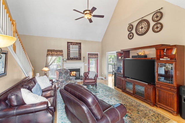 1166 Ben Hill Blvd, Nolensville, TN 37135 - living room featuring high vaulted ceiling, ceiling fan, a warm lit fireplace, light wood finished floors, and stairs
