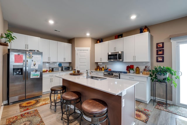 1605 Medinah Ln, Lebanon, TN 37087 - kitchen with appliances with stainless steel finishes, a breakfast bar area, decorative backsplash, white cabinets, and light wood finished floors