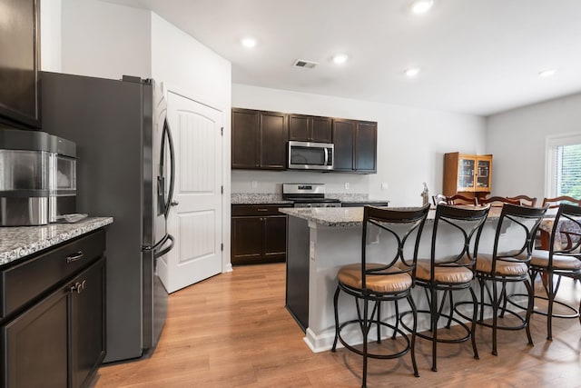 5073 Hunters Village Dr, Lebanon, TN 37087 - kitchen featuring appliances with stainless steel finishes, a breakfast bar, light wood-style flooring, a center island with sink, and light stone countertops