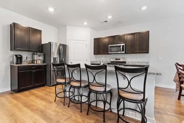 5073 Hunters Village Dr, Lebanon, TN 37087 - kitchen featuring appliances with stainless steel finishes, a breakfast bar, dark brown cabinetry, light wood finished floors, and a center island with sink