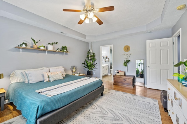 123 Hubbard St, Hohenwald, TN 38462 - bedroom featuring light wood-type flooring, a raised ceiling, ceiling fan, ensuite bathroom, and a textured ceiling