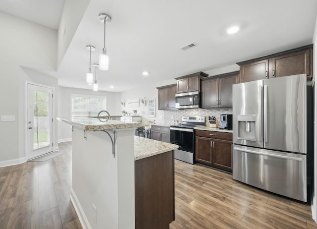 1175 Eagles Nest Ln, Clarksville, TN 37040 - kitchen with stainless steel appliances, dark brown cabinetry, wood finished floors, a kitchen island with sink, and light stone countertops