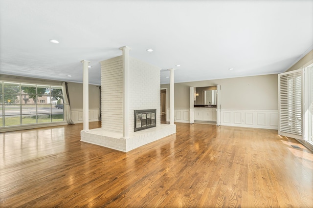 818 N Rutherford Blvd, Murfreesboro, TN 37130 - unfurnished living room with ornate columns, a decorative wall, wood finished floors, a brick fireplace, and a wainscoted wall