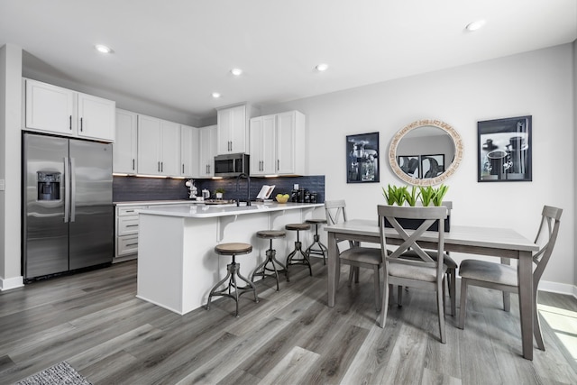 184 Primrose Ln, Gallatin, TN 37066 - kitchen featuring appliances with stainless steel finishes, light wood-style floors, backsplash, a breakfast bar, and a peninsula