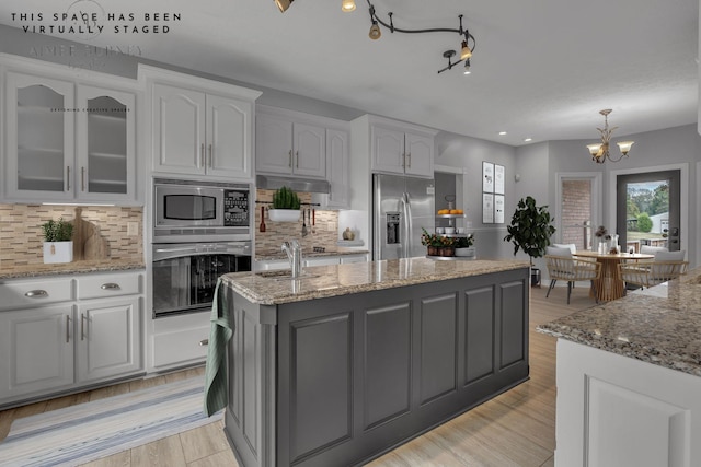 2103 Liebengood Rd, Goodlettsville, TN 37072 - kitchen featuring stainless steel appliances, white cabinetry, an island with sink, a chandelier, and backsplash