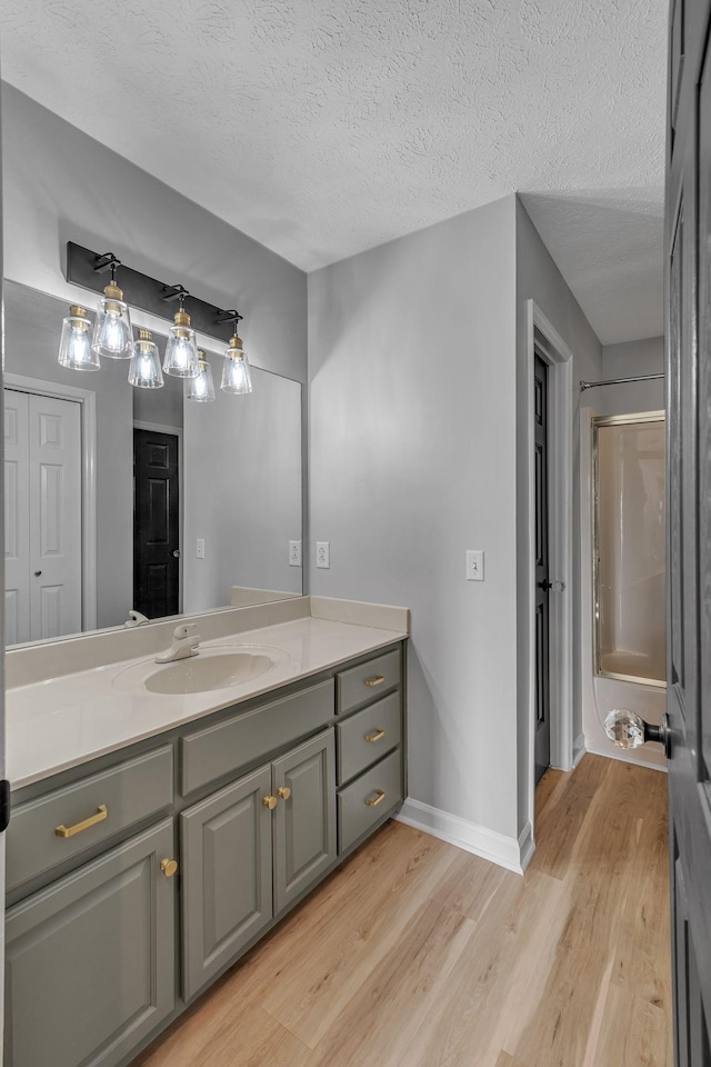 2103 Liebengood Rd, Goodlettsville, TN 37072 - bathroom with wood finished floors, vanity, baseboards, a textured ceiling, and bath / shower combo with glass door