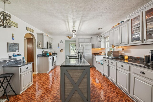 834 Union Camp Rd, Lafayette, TN 37083 - kitchen featuring appliances with stainless steel finishes, arched walkways, a textured ceiling, an island with sink, and glass insert cabinets