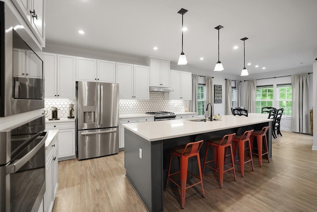 3067 Boxbury Ln, Spring Hill, TN 37174 - kitchen with stainless steel appliances, light wood-style flooring, backsplash, a kitchen island with sink, and a kitchen bar