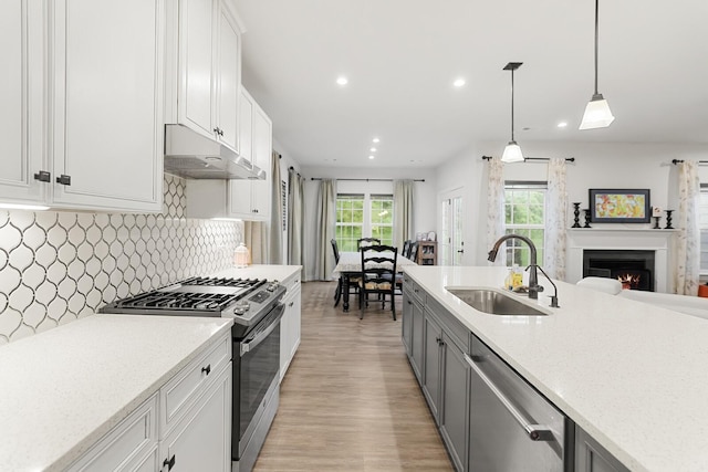 3067 Boxbury Ln, Spring Hill, TN 37174 - kitchen with stainless steel appliances, under cabinet range hood, light wood finished floors, recessed lighting, and a warm lit fireplace