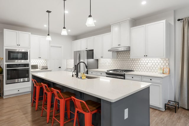 3067 Boxbury Ln, Spring Hill, TN 37174 - kitchen featuring stainless steel appliances, under cabinet range hood, decorative backsplash, a kitchen breakfast bar, and light countertops