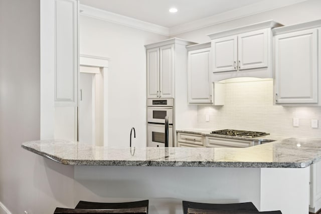 286 Keswick Grove Ln, Franklin, TN 37067 - kitchen with stainless steel gas cooktop, double oven, a breakfast bar area, light stone countertops, and ornamental molding