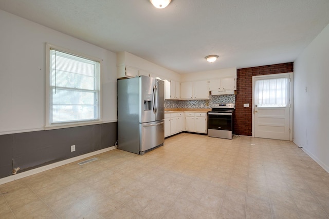 7703 Horn Tavern Rd, Fairview, TN 37062 - kitchen featuring appliances with stainless steel finishes, white cabinetry, light floors, under cabinet range hood, and backsplash