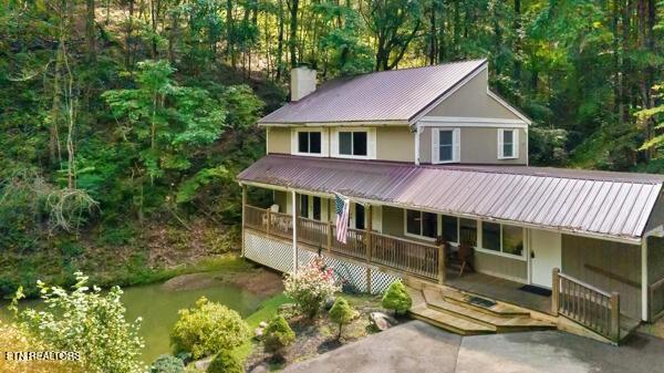 3127 Emerald Springs Loop, Sevierville, TN 37862 - view of front of house with a porch, a chimney, metal roof, a wooded view, and stucco siding