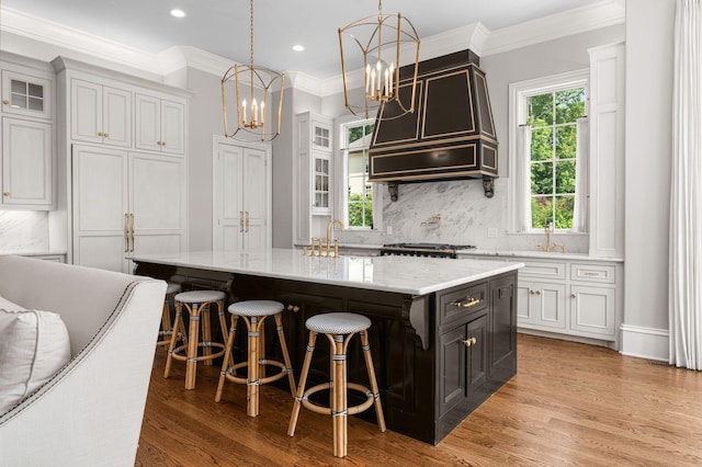 1024 Vaughn Crest Dr, Franklin, TN 37069 - kitchen with a chandelier, a kitchen island with sink, glass insert cabinets, light stone counters, and tasteful backsplash