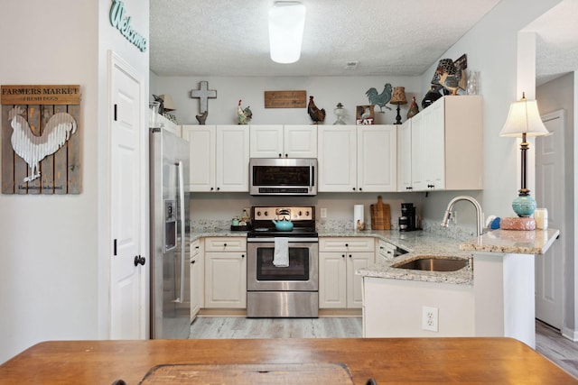 2104 Loudenslager Dr, Thompsons Station, TN 37179 - kitchen with appliances with stainless steel finishes, a peninsula, light wood-style flooring, a textured ceiling, and light stone counters