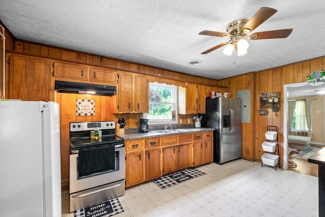 154 Crains Landing Rd, Dover, TN 37058 - kitchen featuring stainless steel appliances, under cabinet range hood, a sink, brown cabinets, and wooden walls